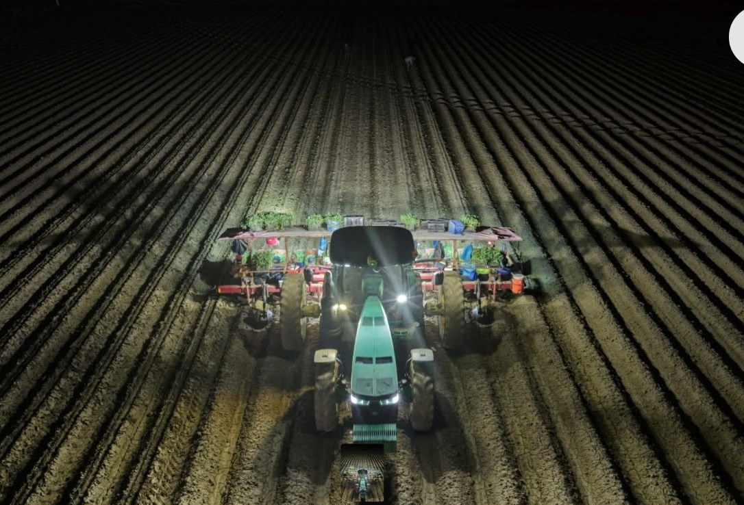 Tractor running a plowed field after dark under work lights during harvest season